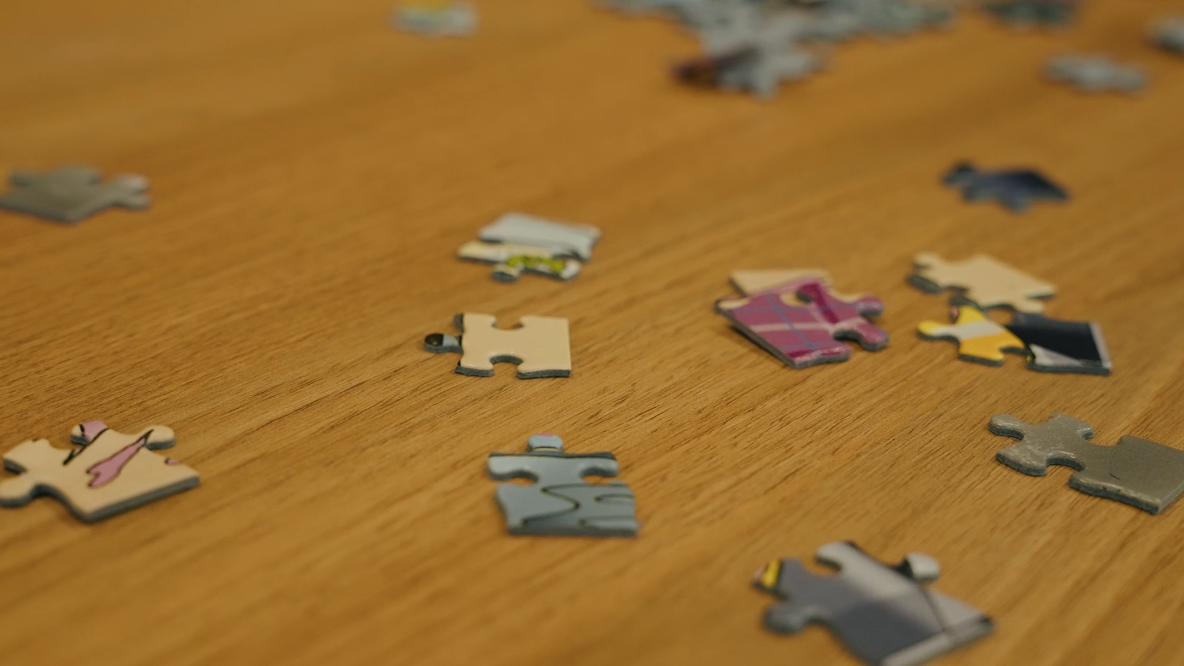 Scattered jigsaw puzzle pieces on a wooden table.